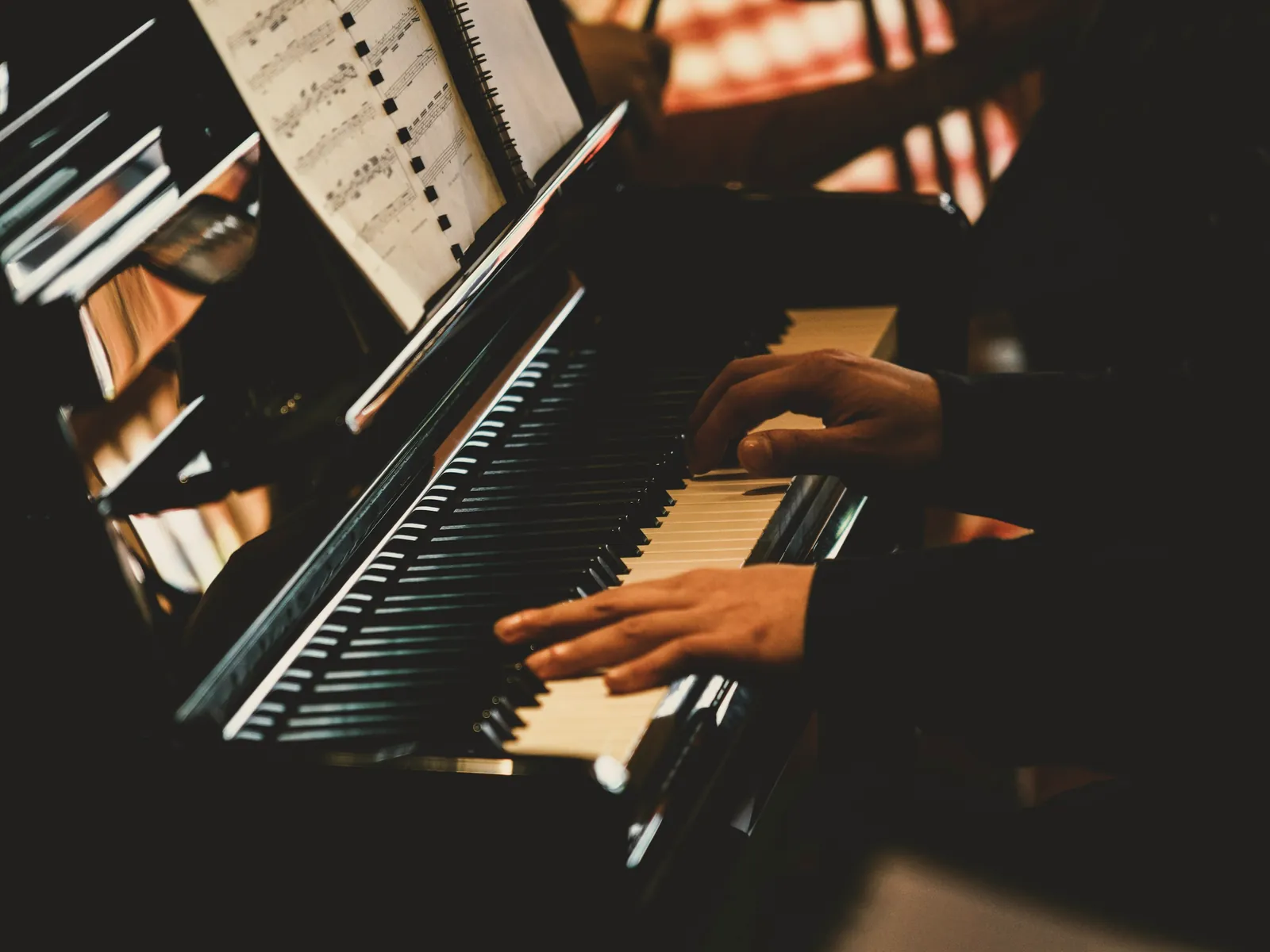 A pianist's hands playing a black grand piano, with sheet music open on the music stand
