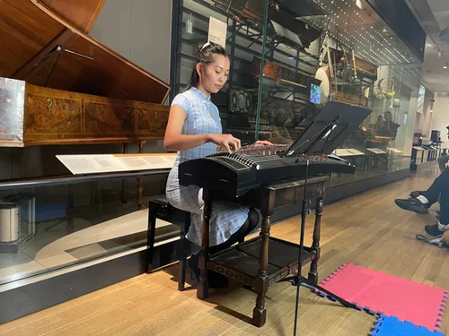 Agnes playing the guzheng among display cases of historic instruments